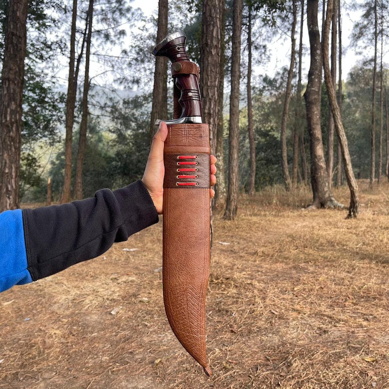 Person holding a large knife with a brown leather sheath in a forest for camping and protection