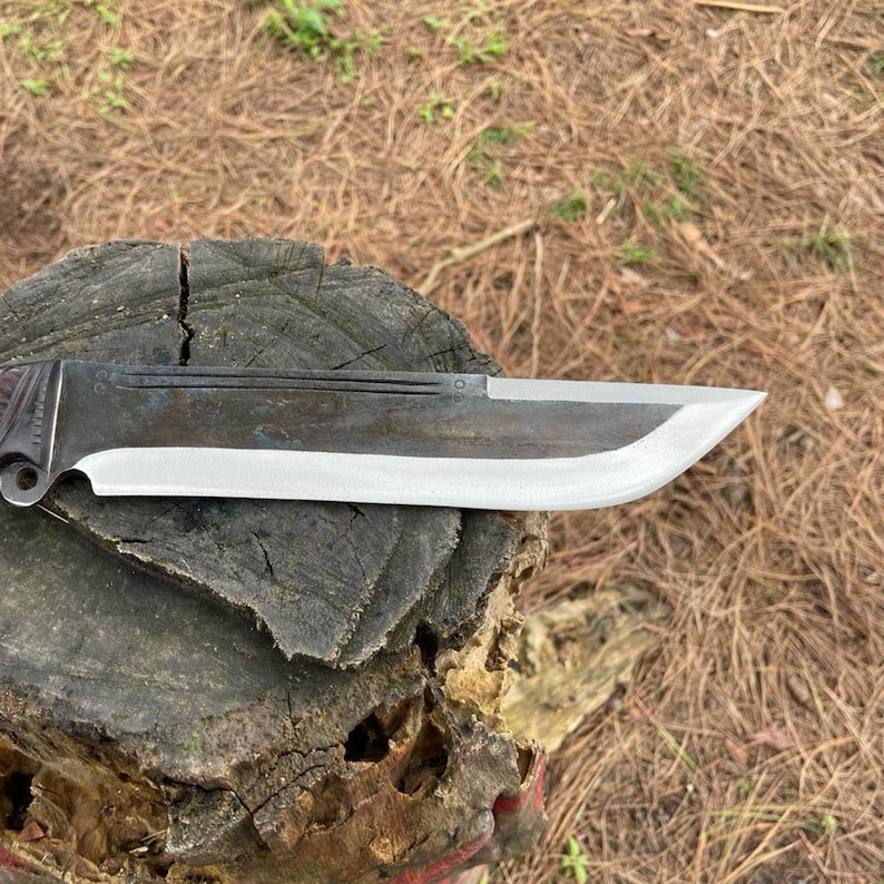 Knife with a black handle and silver blade on a wooden stump for camping and safety.