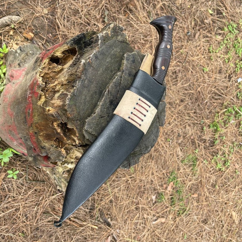 Decorative knife with a black leather sheath for blade protection and wooden handle on a textured surface