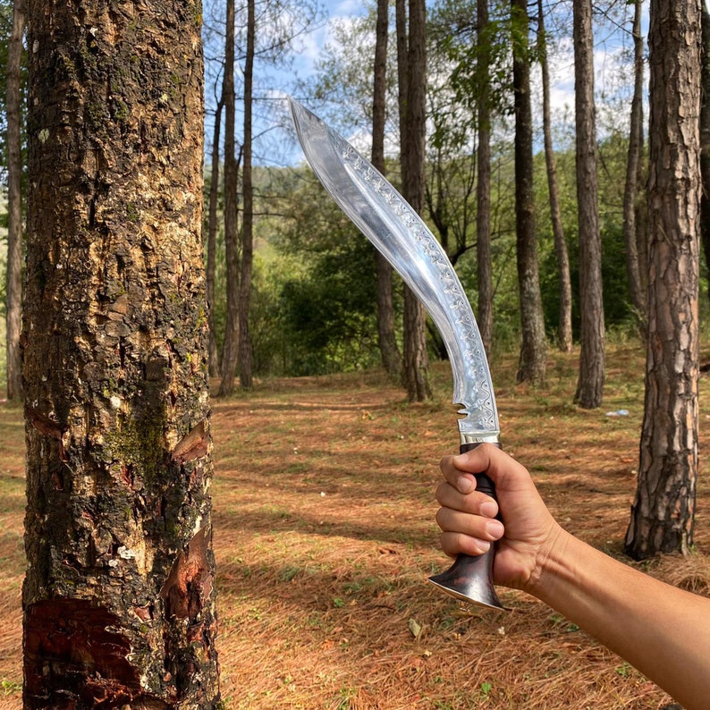 Hand holding a curved salyani kukri near a tree in a forest used for camping and protection