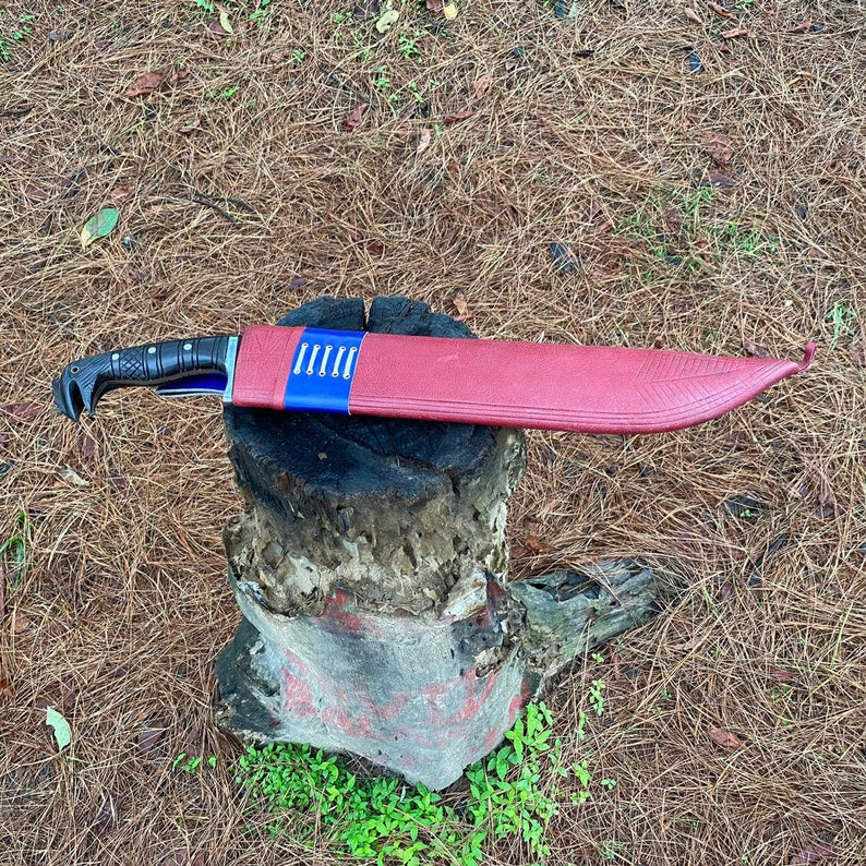 Red leather sheath with machete knife with a black handle on a tree stump in a forest for camping and protection