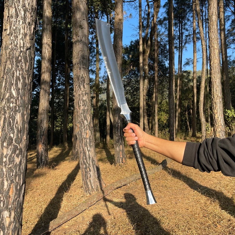 Person holding a large sword in a forest used for camping and protection form wildlife