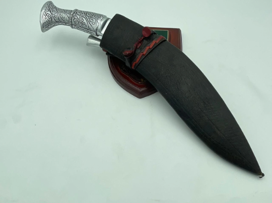 A 12 inch hand forged kukri with a polished blade and a brass handle, accompanied by a black leather scabbard. The knife is displayed on a white background.