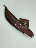 A 10 inch hand forged Bowie knife with a black and gray blade and a brown rosewood handle, displayed next to its scabbard.