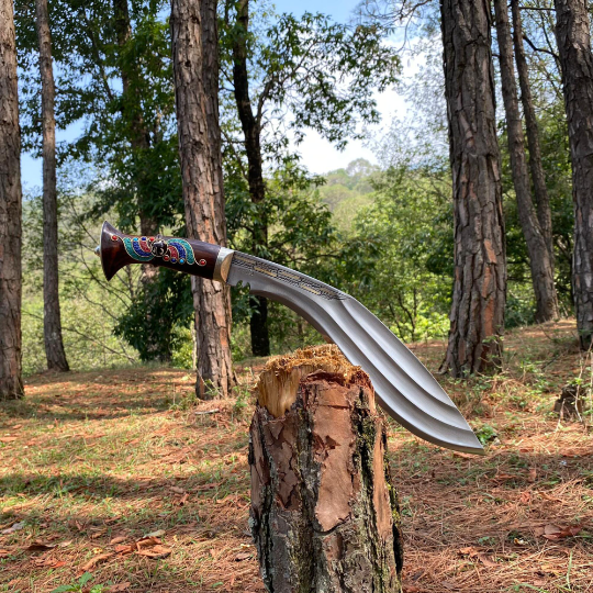 A 10 inch Farmer 3 Chirra Kukri knife with a hand-bitten Gurkha blade design, resting on a wooden stump in a natural outdoor setting with trees in the background.