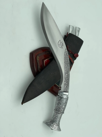 A 12 inch hand forged kukri with a polished blade and a brass handle, accompanied by a black leather scabbard. The knife is displayed on a white background.