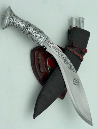 A 12 inch hand forged kukri with a polished blade and a brass handle, accompanied by a black leather scabbard. The knife is displayed on a white background.