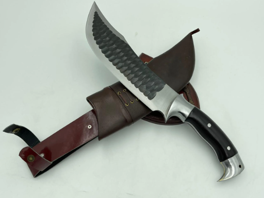 A 10 inch hand forged Bowie knife with a black and gray blade and a brown rosewood handle, displayed next to its scabbard.