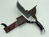 A 10 inch hand forged Bowie knife with a black and gray blade and a brown rosewood handle, displayed next to its scabbard.