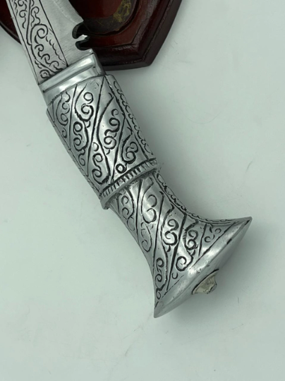 A 12 inch hand forged kukri with a polished blade and a brass handle, accompanied by a black leather scabbard. The knife is displayed on a white background.