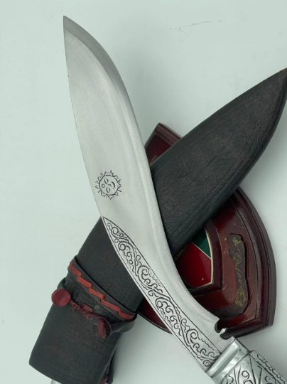 A 12 inch hand forged kukri with a polished blade and a brass handle, accompanied by a black leather scabbard. The knife is displayed on a white background.
