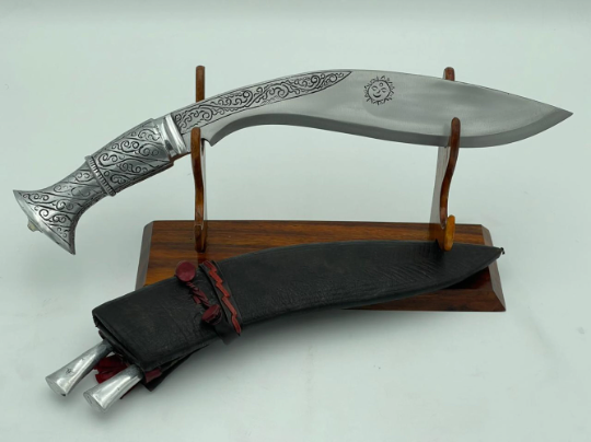 A 12 inch hand forged kukri with a polished blade and a brass handle, accompanied by a black leather scabbard. The knife is displayed on a white background.