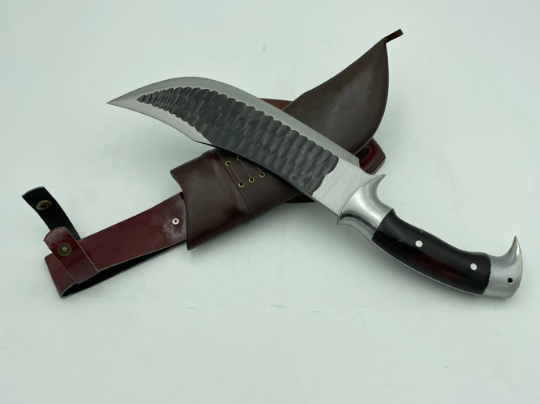 A 10 inch hand forged Bowie knife with a black and gray blade and a brown rosewood handle, displayed next to its scabbard.