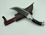 A 10 inch hand forged Bowie knife with a black and gray blade and a brown rosewood handle, displayed next to its scabbard.