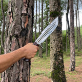 Hand holding a sword against a tree in a forest setting