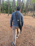 Person walking in a forest carrying a rifle on their back
