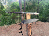 Two large knives on a wooden block against a forest background