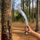 Hand holding a curved salyani kukri near a tree in a forest used for camping and protection