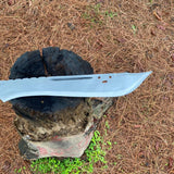 Metal machete blade on a tree stump with dry grass in the background used for camping and protection