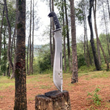 Large machete knife with a black handle on a wooden stump in a forest for camping and protection