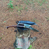 Two knives on a tree stump with a natural outdoor background with its leather sheath as well for cover