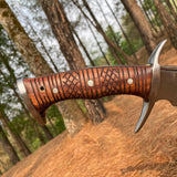 Wooden-handled knife with intricate patterns against a forest background