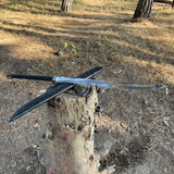 Two swords crossed on a wooden stump in an outdoor setting with grass and trees.