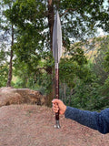 Person holding a large viking spear outdoors with trees in the background