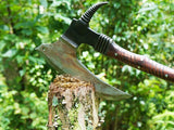 Decorative axe with a curved blade and wooden handle on a tree stump against a green forest background.